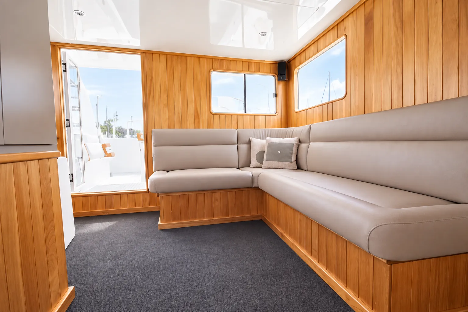 Corner lounge on Kiwa II with leather seating, timber panelling and a door to the deck