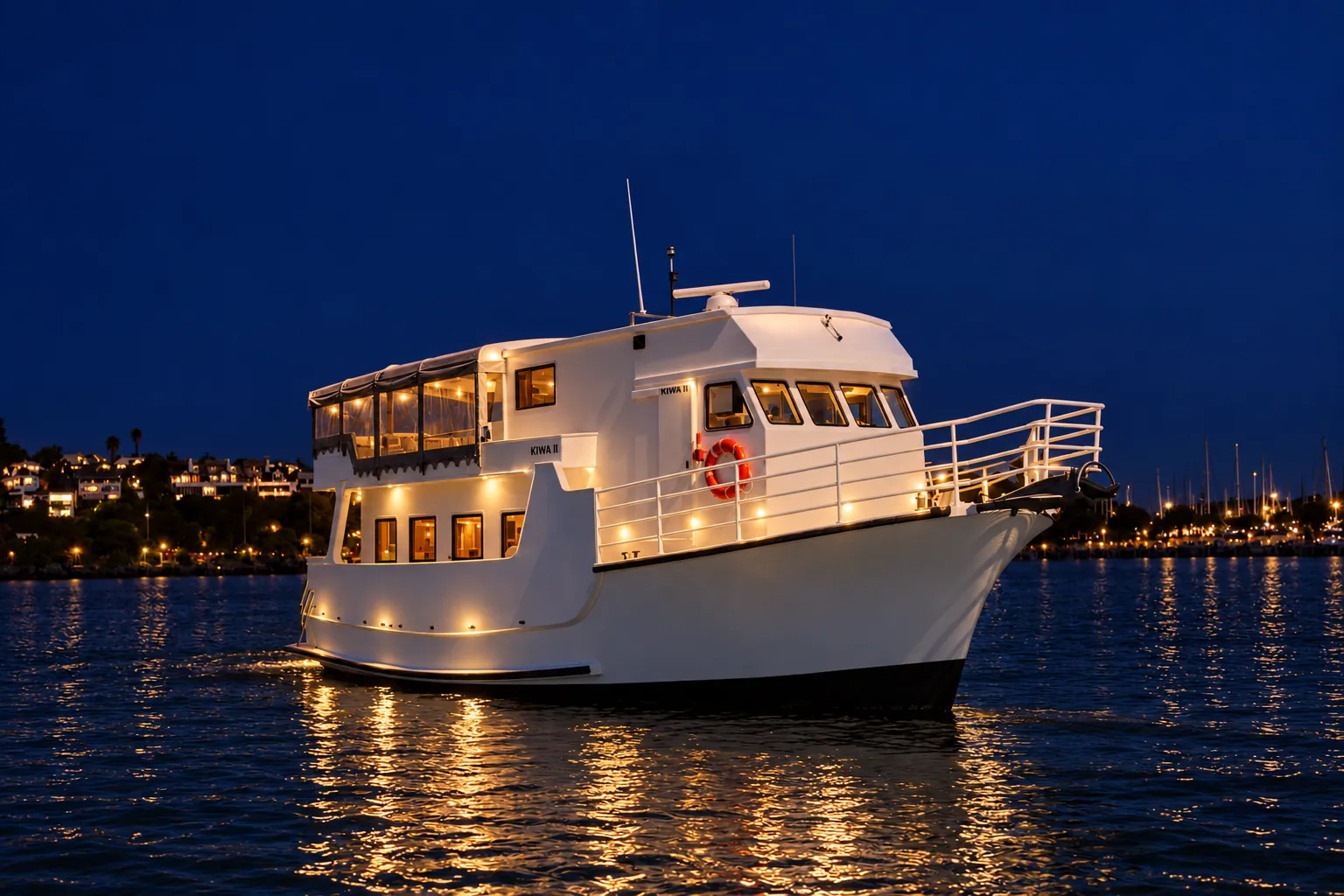 Kiwa II lit up at night on Auckland Harbour, with marina and hillside lights behind